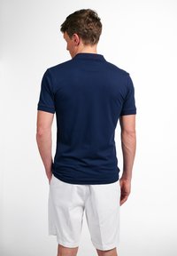Donkerblauwe polo shirt, korte mouwen, van katoen, klassieke kraag, achterkant zicht; gedragen met witte shorts, gladde textuur, minimale details.