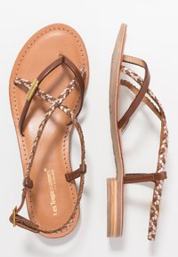 Sandales en cuir brun avec des lanières tressées, semelle plate, détails cousus et accents métalliques. Design minimaliste avec ajustement réglable.