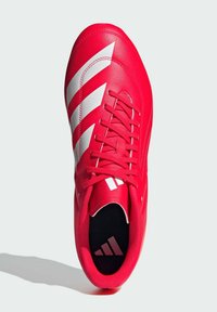 Zapatilla deportiva roja con un acabado de cuero liso, que presenta acentos de tres rayas blancas, un cierre con cordones y una planta interior texturizada negra.