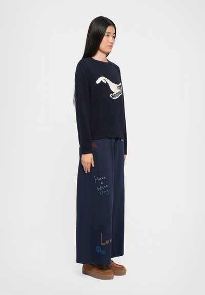 Navy knit sweater with white and black graphic; paired with navy wide-leg pants featuring colorful text and accents; brown platform shoes.