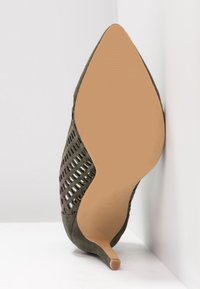 Szpilka w kolorze oliwkowej zieleni, z zaostrzonym noskiem, wykonana z zamszowego materiału, z wycięciami w designie. Ma gładką beżową podeszwę i wąski obcas.