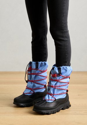 Sorte og blå vandtætte støvler med røde snørebånd, der har et højt ankeldesign og robuste såler til godt greb, velegnede til udendørs brug.