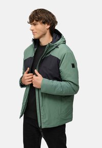 Grøn og sort tofarvet zip-up jakke med hætte, letvægtsmateriale, for- og baglommer samt justerbar hætte med snore.