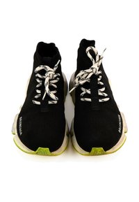 Paire de baskets montantes noires avec des lacets blancs et noirs, des semelles blanches épaisses, des bouts verts et le logo Balenciaga sur les côtés.