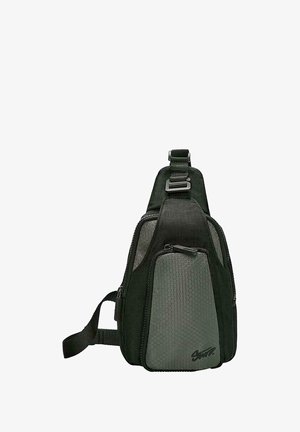 Sötétzöld sling táska háromszög alakban, texturált hatszögletű díszítéssel, állítható pánttal és elülső cipzáras zsebbel.