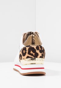 Weiße Sneaker mit Leo-Print am Rücken, goldenen Akzenten und einer strukturierten Ferse. Sohle mit rot-weißen Streifen. Weiches Material mit einem eleganten Design.