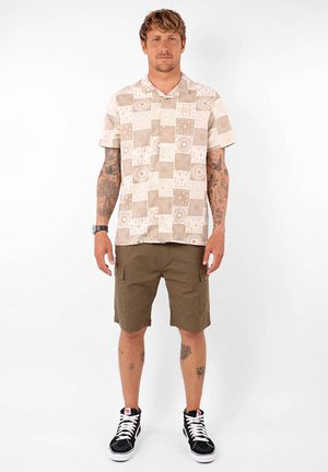 Chemise à manches courtes avec un motif de patchwork beige, portée avec un short cargo olive, associée à des baskets montantes noir et blanc.