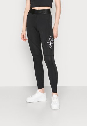 Leggings noirs avec une taille haute, arborant un logo blanc et des accents de design angulaires, fabriqués à partir d'un tissu extensible. Portés avec des baskets blanches.