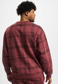 Weinrote Sweatshirt mit schwarzem Karomuster. Weiche Textur, gerippte Bündchen und Rundhalsausschnitt. Die Rückansicht zeigt das gesamte Design.