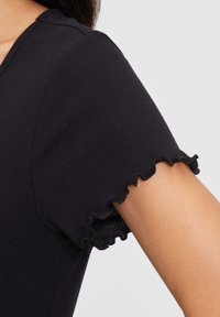Black ribbed top featuring short sleeves with ruffled edges. The fabric has a soft texture, highlighting the sleek design and clean lines.