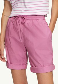 Shorts en coton rose avec une taille élastique, cordon de serrage ajustable, poches latérales et ourlets retroussés. Texture lisse et design décontracté.