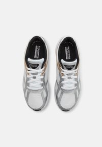 Chaussures de sport blanches avec des accents gris et un revêtement noir. Tige en mesh, bouts ronds et semelles plates à texture. Comprend des lacets et un logo sur la languette.