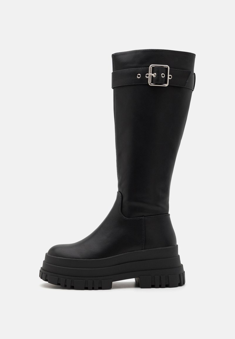 Botas negras hasta la rodilla hechas de cuero suave, con una suela de goma gruesa y un acento de hebilla de metal en la correa superior.