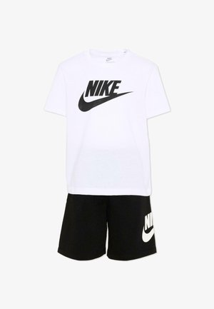 Camiseta blanca de manga corta de Nike con un gran logo negro, combinada con pantalones cortos negros que llevan un logo blanco de Nike en la pierna izquierda.