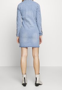 Vestido de mezclilla con mangas largas, color azul claro, silueta ajustada y costuras en la espalda. Combinado con botas de tobillo de textura y estampado de serpiente.