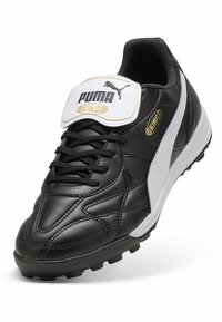 Zapatilla deportiva de cuero negra con detalles en blanco y branding dorado. Presenta un cuello acolchado, diseño con cordones y suela de goma texturizada.