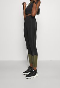Completo activewear nero e oliva composto da un top corto e leggings a vita alta, con una finitura testurizzata e un blocco di colore a contrasto sulla gamba.