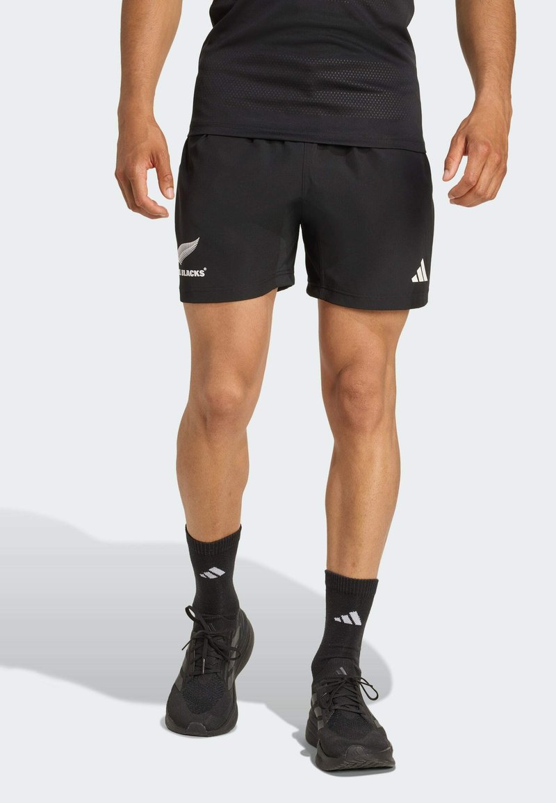Zwarte sportieve shorts met een elastische tailleband, voorzien van witte logo-accenten. Gecombineerd met zwarte sokken en hardloopschoenen, wat een sportieve stijl benadrukt.