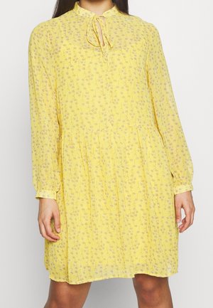 Żółta sukienka w kwiaty z długimi rękawami, zapinana na guziki z wiązaniem przy dekolcie. Lekka, fakturowana tkanina o luźnym kroju.