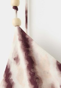 Gros plan d'un tissu tie-dye beige et marron avec une fine lanière comportant deux perles en bois clair sur fond blanc uni.