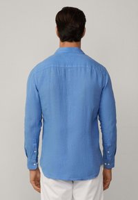 Světle modrá lněná košile s dlouhými rukávy, špičatým límcem, manžetami na knoflíky a jemnou texturou. Přiléhavý střih, delší zadní lem.