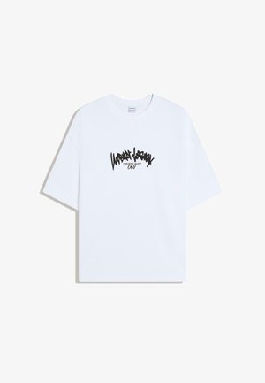 Witte oversized T-shirt met korte mouwen, bedrukt met zwarte graffiti-achtige tekst "Urban Legacy" en kleinere tekst "007" in het midden vooraan.