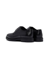 Par de zapatos de vestir para hombre de cuero negro con cordones y suelas de goma gruesa, fotografiados desde el lado trasero sobre un fondo blanco.