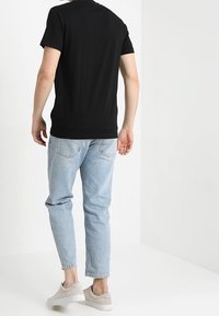 Černé bavlněné tričko, volný střih, spárováno se světle modrými džíny. Šedé tenisky s hladkou texturou, zobrazené zezadu.