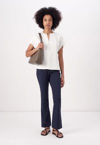 Haut blanc à manches courtes avec un décolleté en trou de serrure, pantalon évasé bleu marine et sandales noires. Sac à main gris au toucher lisse.