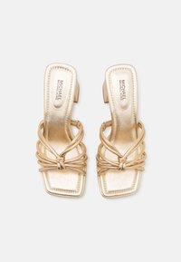 Gylne høyhælte sandaler med firkantet tå, med sammenflettede remmer og en liten hæl. Materialet har en skinnende, metallisk finish.
