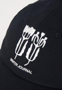 Black cap featuring white embroidered floral design and "WINTER JOURNAL" text. Smooth texture with a structured shape and vent at the crown.