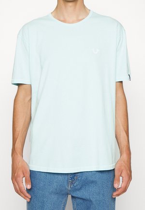 T-shirt en coton bleu clair avec un col rond, des manches courtes et un petit logo blanc sur la poitrine. Coupe décontractée, texture douce.