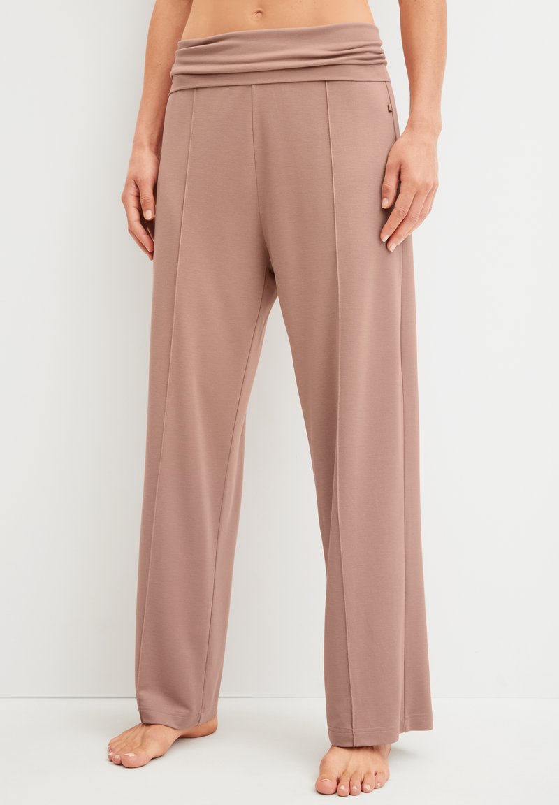 Femme portant un pantalon mauve taille haute à jambes larges avec des coutures frontales, debout pieds nus sur un fond blanc uni.
