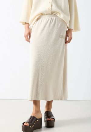 Kremowa spódnica midi z elastycznym pasem, o delikatnej fakturze. Dobrana do ciemnobrązowych sandałów na platformie z wzorem krokodyla.