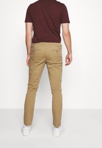 Khaki trousers with a slim fit, featuring back pockets and a smooth texture, paired with a maroon short-sleeve shirt and white sneakers.