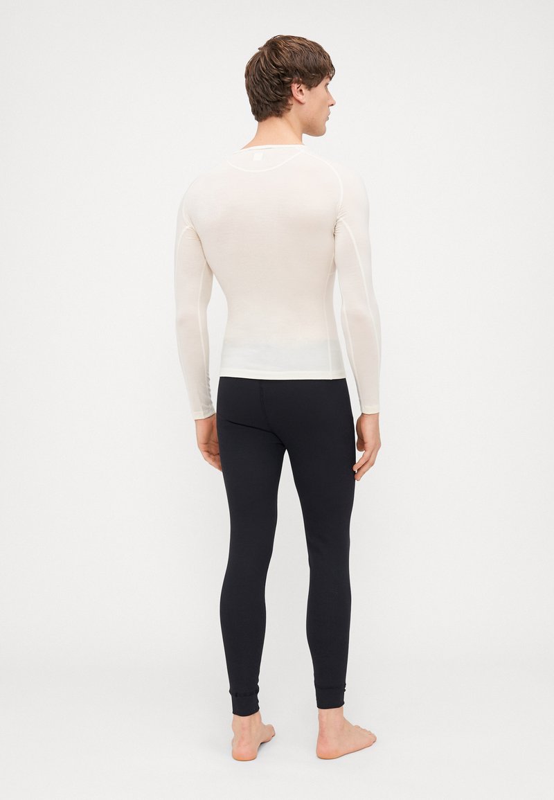 Maglietta leggera a maniche lunghe di colore avorio, abbinata a leggings neri aderenti. Texture liscia e vestibilità atletica, senza loghi o motivi visibili.