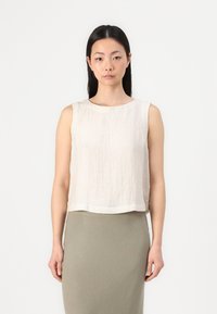 Top corto senza maniche in tessuto leggero e testurizzato di colore beige con scollatura rotonda, abbinato a una gonna aderente nei toni neutri.