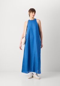 Lång, ärmlös klänning i blått linne med en avslappnad passform och slät textur. Bärs med vita sneakers och en liten axelväska.