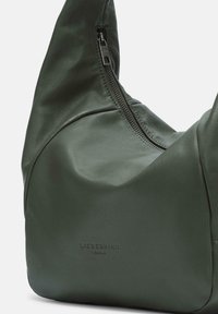 Zielona skórzana torba o miękkiej, teksturowanej powierzchni, z zamknięciem na zamek błyskawiczny i zaokrąglonym kształtem. Wytłoczone logo z przodu.