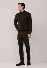 Ciemnozielony golf z grubym splotem warkoczowym, zestawiony z ciemnozielonymi zwężanymi spodniami, dopełniony brązowymi botkami za kostkę. Gładka faktura, dopasowany krój.