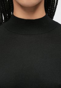 Top nero a collo alto a coste con design aderente e texture liscia e morbida. Presenta un collo alto e dettagli di cuciture minimi.