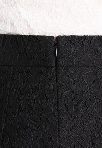 Černá krajková látka s květinovými vzory, s viditelným zipem na zadní straně. Textura je složitá a mírně vystouplá.