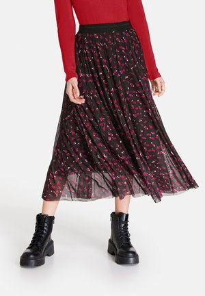 Jupe midi plissée noire avec des motifs abstraits rose et violet, taille élastique, associée à des bottes chunky noires à lacets.