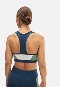 Sujeción deportiva en color navy con diseño de espalda nadadora. Presenta acentos en color verde y blanco, y una banda texturizada. Tejido suave, estilo ajustado.