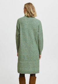 Abito in maglia a maniche lunghe di una morbida tonalità di verde miscelato. Presenta una silhouette rilassata, orlo a coste e un design lungo fino al ginocchio con una finitura testurizzata.