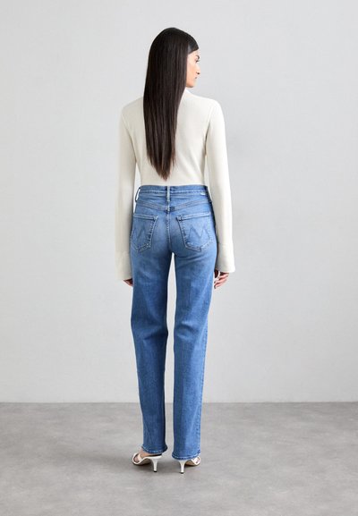 Blue high-waisted jeans with a straight leg design, featuring back pockets and stitching details. The model wears a ribbed white top.