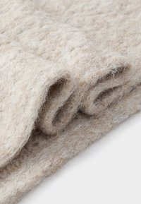 Gros plan sur un tissu en laine beige doux et tricoté, avec une texture duveteuse et des boucles visibles sur un bord plié.