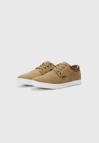 Brown suede sneakers with white rubber soles, lace-up design, rounded toe, and a contrasting tan accent at the heel.