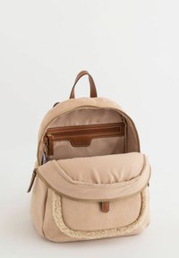 Beiger Stoffrucksack mit einer strukturierten, weichen Front, goldenem Reißverschluss, braunen Lederakzenten und einem geräumigen Innenraum mit einer Reißverschlusstasche.