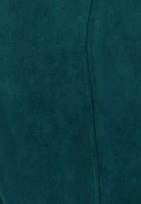 Gros plan sur un tissu suédé bleu sarcelle foncé avec des coutures de couture verticales visibles.